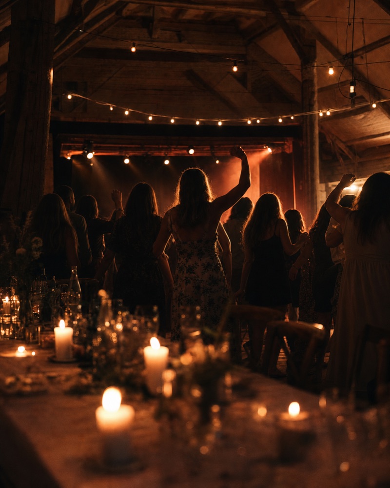 Gæster danser til bryllupsfest i lade med lyskæder